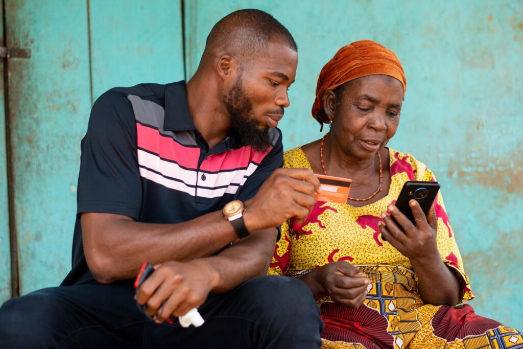 Mother and son sitting together, with the son helping his mother make a payment on her phone