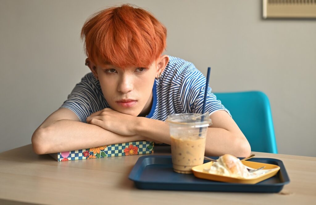 Young person sitting solemnly with arms resting on a table, looking thoughtful