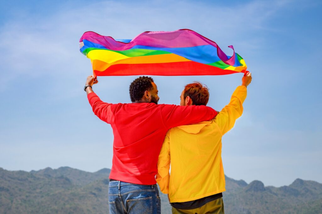 Two men embracing while holding a rainbow flag, showing support for LGBTQ+ rights