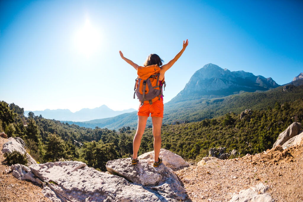 Woman standing on a mountain, arms raised in the air, overlooking the view