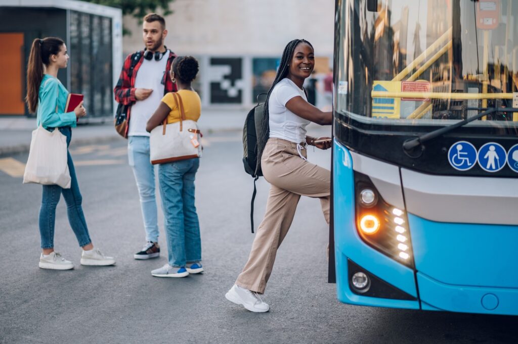 Young woman getting on a bus, carrying a bag and preparing to board