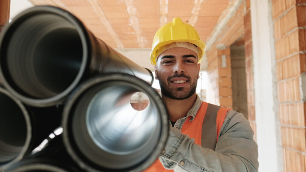 Young workman wearing a safety hat, carrying construction materials and smiling
