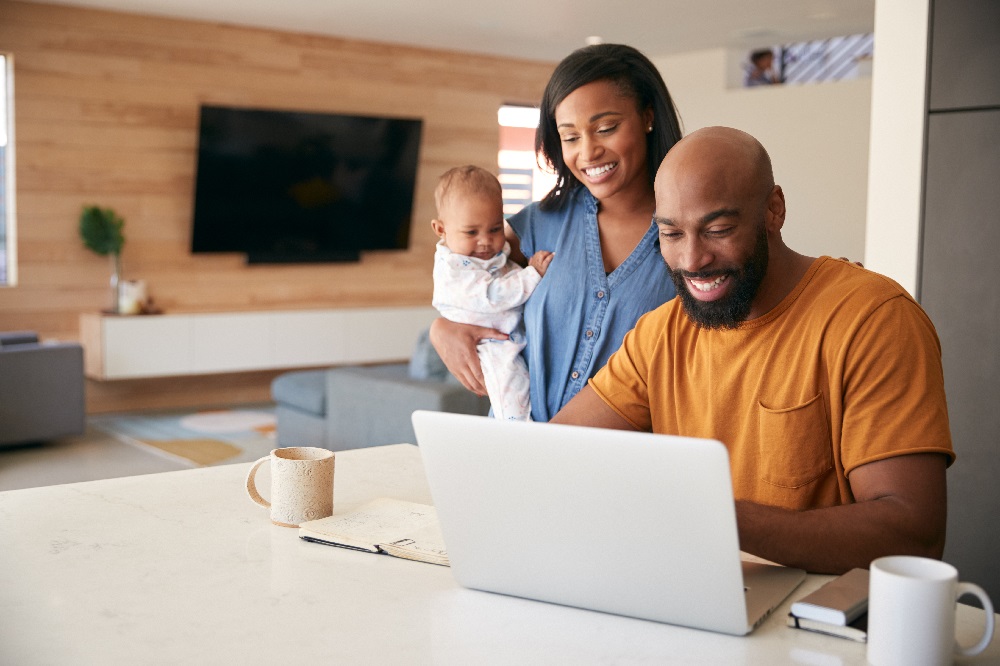 A couple at a laptop with the woman holding a baby.